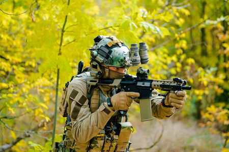 Airsoft man in uniform, stand with machine gun on yellow forest backdrop. Soldier aims at the sight.の写真素材