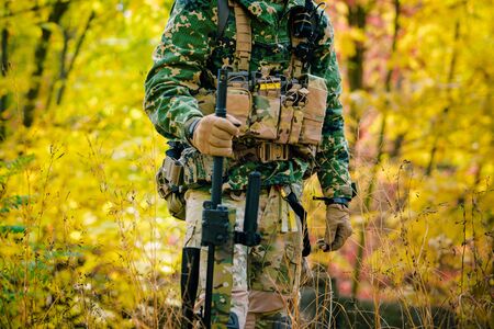 Airsoft, Part of amunition of man in uniform stand with sniper rifle on autmn forest background. Side view.の写真素材