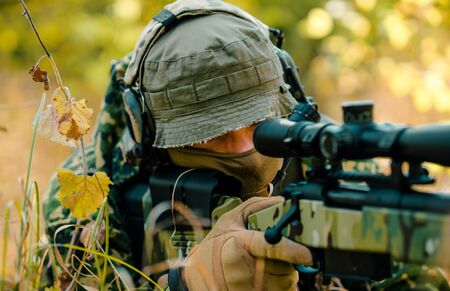 Closeup man in uniform with sniper rifle. Airsoft soldier lay in long grass and aims at the sight.の写真素材