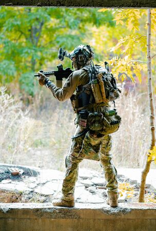 Man in uniform with machine gun on forest background. Airsoft soldier aims at the sight. Vertical photo.の写真素材