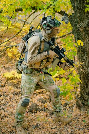 Airsoft man in uniform beside tree move with machine gun. Side view. Vertical photo.の写真素材