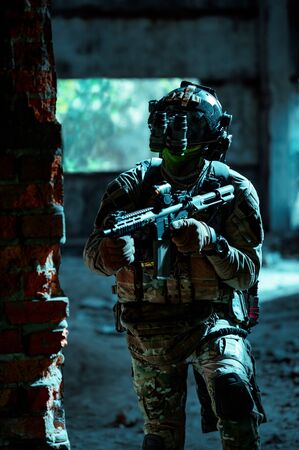 Man in uniform with machine gun and night-vision device move inside broken building. Airsoft soldier in night building.の写真素材