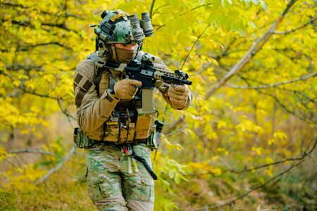 Airsoft man in uniform, move with machine gun on yellow forest backdrop. Soldier aims at the sight.の写真素材
