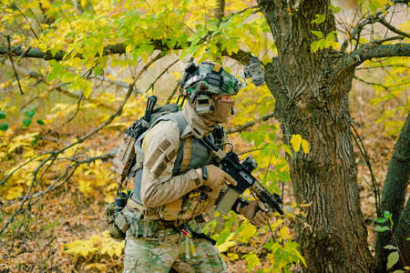 Airsoft man in uniform beside tree move with machine gun. Side view.の写真素材