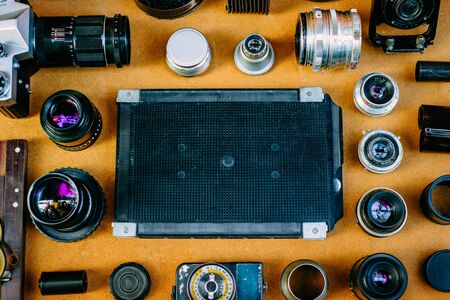 Retro mockup, Black retro plastic box for film in center of retro vintage photographic accessories and quipments around on wooden Background. Top viewの写真素材