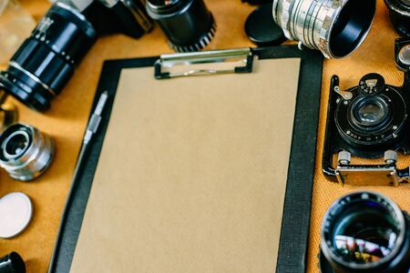 Closeup retro mockup, Clip board with paper with retro vintage photographic accessories and quipments around on wooden Background. の写真素材