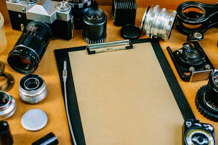 Closeup retro mockup. Clip board with paper with retro vintage photographic accessories and quipments around on wooden Background.の写真素材