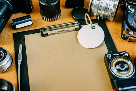 Retro photographic mockup. Closeup paper round label on clip board with retro vintage photographic accessories and quipments around on wooden Background.の写真素材