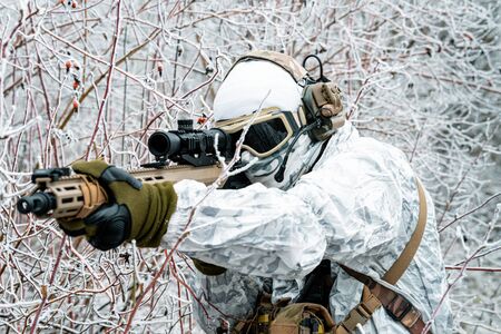 Closeup military man in white camouflage uniform with machinegun. Soldier in the winter forest and aims at the sight of the machinegun. Side viewの写真素材