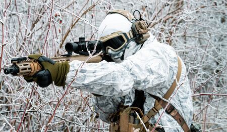 Closeup military man in white camouflage uniform with machinegun. Soldier  in the winter forest and aims at the sight of the machinegun. Side viewの写真素材