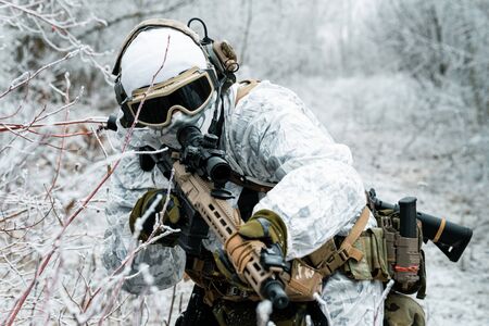 Closeup military man in white camouflage uniform with machinegun. Soldier sneaking in the winter forest with machinegun. Front viewの写真素材