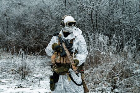 Military man in white camouflage uniform with machinegun. Soldier in the winter forest territory background. Horizontal photoの写真素材