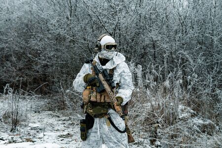 Military man in white camouflage uniform with machinegun. Soldier in the winter forest territory background. Horizontal photoの写真素材