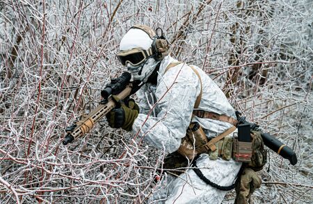 Military man in white camouflage uniform with machinegun. Soldier sneaking in the winter forest with machinegun. Side viewの写真素材