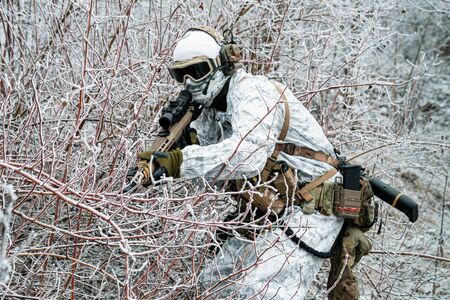 Military man in white camouflage uniform with machinegun. Soldier sneaking in the winter forest with machinegun. Side viewの写真素材