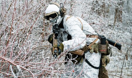 Military man in white camouflage uniform with machinegun. Soldier sneaking in the winter forest with machinegunの写真素材