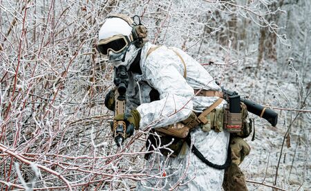 Military man in white camouflage uniform with machinegun. Soldier sneaking in the winter forest with machinegun.の写真素材