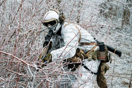 Military man in white camouflage uniform with machinegun. Soldier sneaking in the winter forest with machinegun.の写真素材