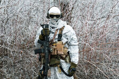 Military man in white camouflage uniform with machinegun. Soldier in the winter forest territory background. Horizontal photoの写真素材