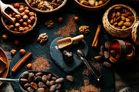 Chocolate candy on stand from blackstone in heart shape with cocoa beans, cinnamon, nuts, cocoa powder around. Chocolate candy with sesame on top.の写真素材
