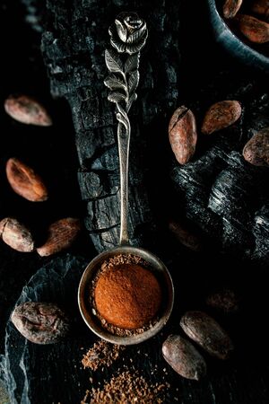 Handmade chocolate candies lay on cocoa powder in spoon on smut. Truffles lay on charcoal on blackstone stand.の写真素材