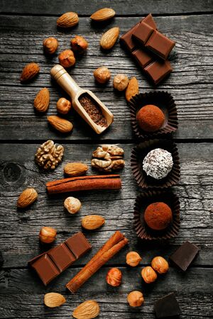 Handmade candies, two truffles with cocoa powder and one with coconut flakes. Chocolate candies inside of candy wrapper on wood table stand with nuts, broken chocolate, cocoa powder and almond around. Top viewの写真素材