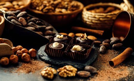 Handmade chocolate candies inside of candy wrappers on stand from blackstone in heart shape. Chocolate candies with nuts on top, cocoa beans, cinnamon, nuts, cocoa powder around.の写真素材