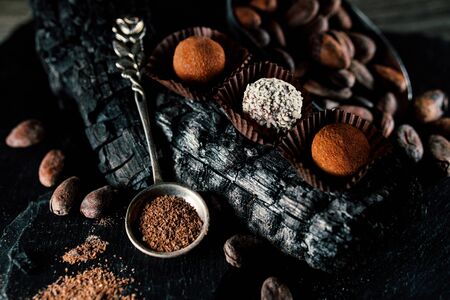 Handmade chocolate candies inside of candy wrappers on smut. Truffles lay on charcoal, with cocoa powder in spoon on blackstone standの写真素材
