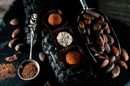 Handmade chocolate candies inside of candy wrappers on fire brand. Truffles lay on charcoal, with...