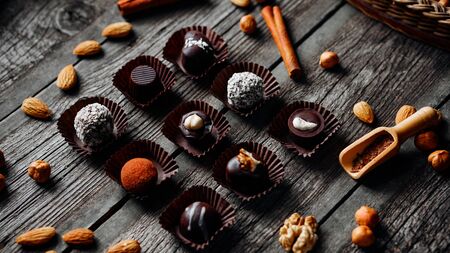 Nine handmade chocolate candies inside of candy wrappers on vintage wooden background. Nuts, cinnamon, almond, husel nut around.の写真素材