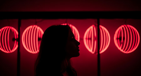 Silhouette of a young woman in front of a red neon lightsの素材