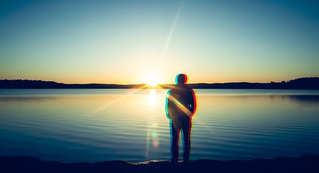 Silhouette of a man standing on the lake and looking at the sunsetの素材