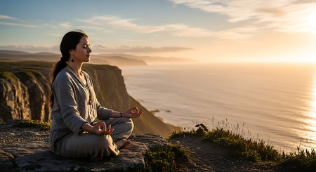 Young woman meditating in lotus position on top of a mountain at sunsetの素材