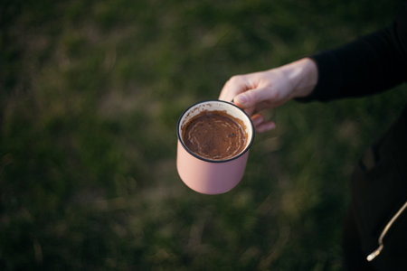 Female hand holding a cup of hot chocolate on a background of green grassの写真素材