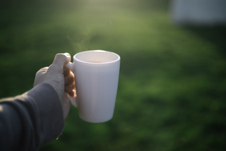 Female hand holding a white cup of coffee on the green grass background