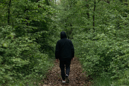 Back view of a man in a black jacket walking in the forestの写真素材