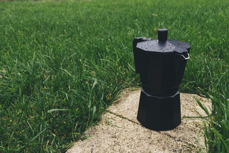 A black plastic coffee maker on a green lawn in the park.の写真素材