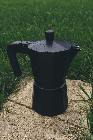 Black coffee maker standing on a concrete path in the grass.の写真素材