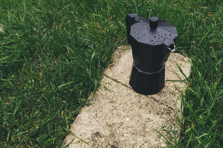 Black coffee maker on a stone in the green grassの写真素材