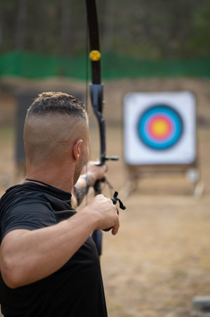 A man is practicing archery in a field. He is holding a bow and arrow and aiming at a targetの写真素材