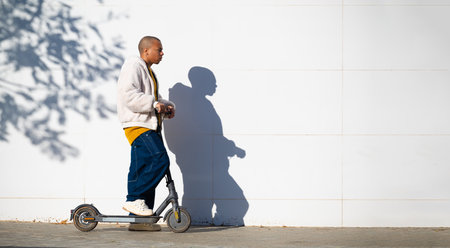 Young man riding electric scooter in the city next to white wallの写真素材