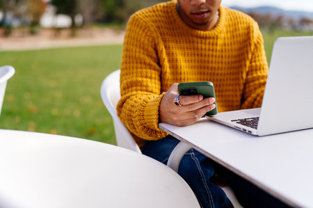 Young black man using laptop and smart phone while working remotely in a parkの写真素材
