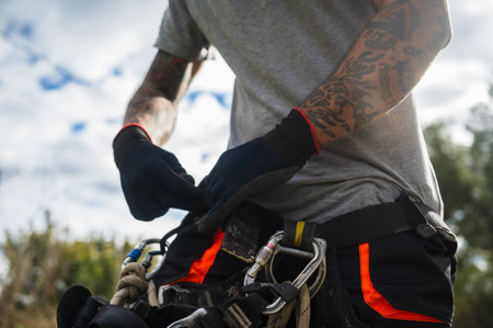Rope access technician wearing gloves and harness preparing for tree pruningの写真素材