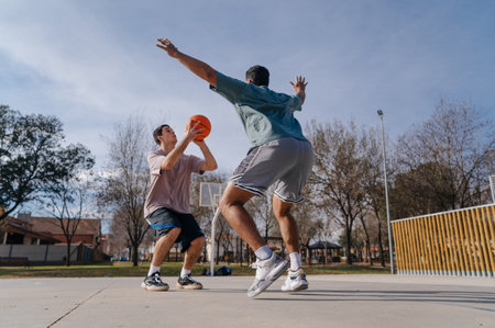 Two friends playing basketball on outdoor court on sunny dayの写真素材