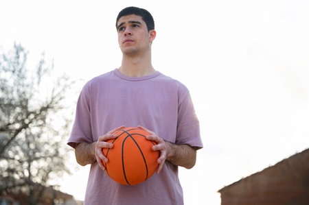Young man holding a basketball, strategizing his next move in a street game, showing urban sport and youthful energyの写真素材