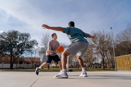 Two friends playing basketball at a street court on a sunny day, enjoying a friendly competitionの写真素材