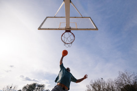 Man dunking during a basketball match outdoors in a sunny dayの写真素材