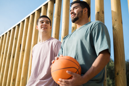 Two male friends taking a break during basketball practice on a sunny dayの写真素材