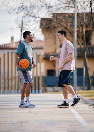 Two friends enjoying a friendly basketball game, talking and smiling on an outdoor courtの写真素材
