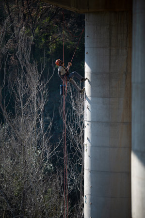 Rope access technician working on bridge pillar, installing anchorages for maintenance or inspectionの写真素材